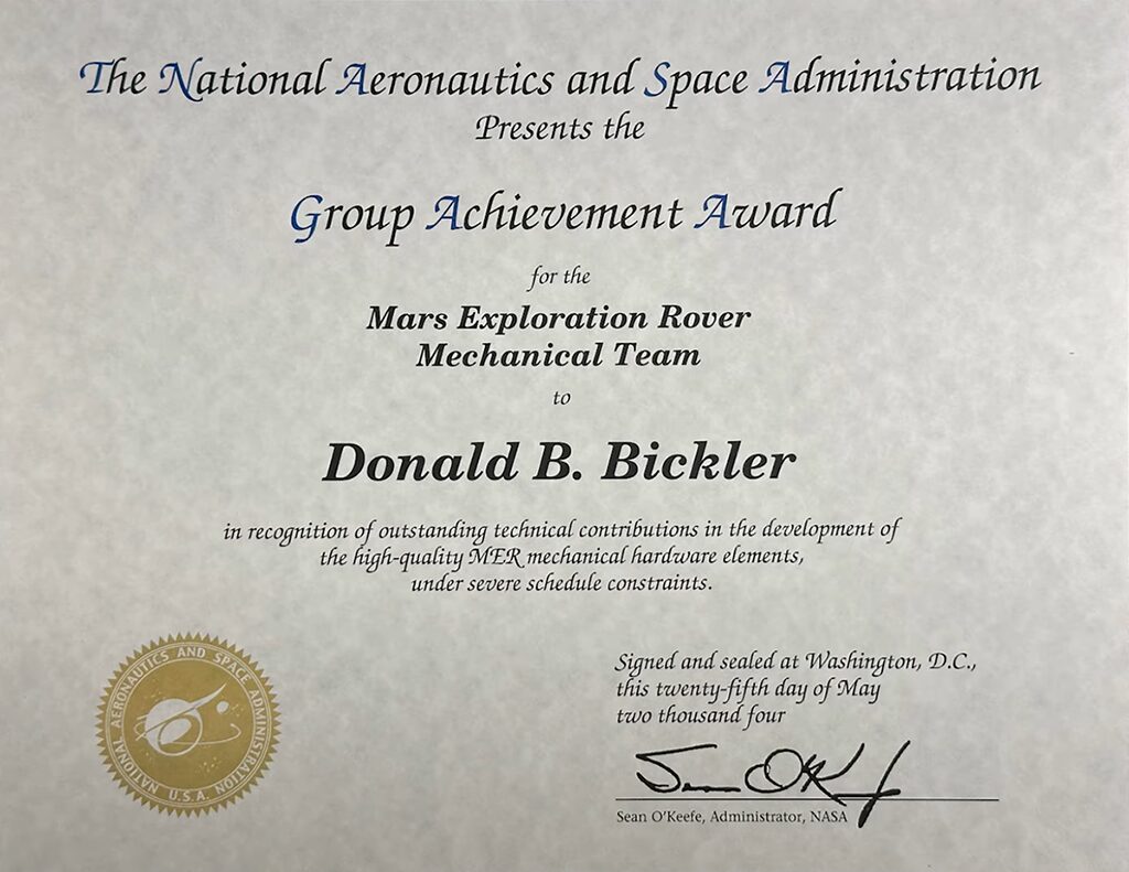 Group Achievement Award has a golden seal at the bottom-left corner containing a text-free version of the "meatball" logo. It is otherwise visually unrecognizable as a NASA document. Printed on parchment paper and employing a decorative font, it resembles a DIY wedding announcement.